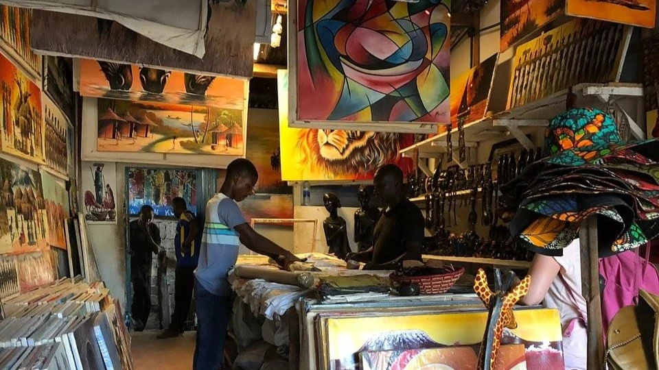 A man standing in front of a store adorned with paintings on the walls of Art and Handicrafts


