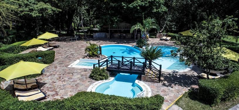 A pool at Sarova Mara Game Camp, surrounded by lush green trees and umbrellas.