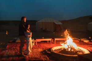 Couple hug in love near big campfire. Romantic night in glamping desert camp in Sahara, Morocco. Honeymoon.