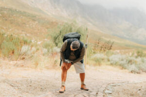 Man mountain hiking, knee pain exercise injury and old caucasian person workout walk alone in Texas desert nature. Massage sore leg muscle, medical emergency and first aid physiotherapy break