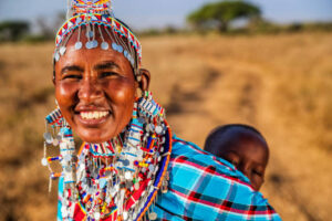 African mother from Masai tribe carrying her baby , Kenya, Africa. Mount Kilimanjaro on the background, central Kenya, Africa. Maasai tribe inhabiting southern Kenya and northern Tanzania, and they are related to the Samburu.