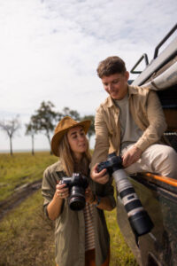 Happy couple of tourists looking at photos on their DSLR cameras during safari travel in national reserve.