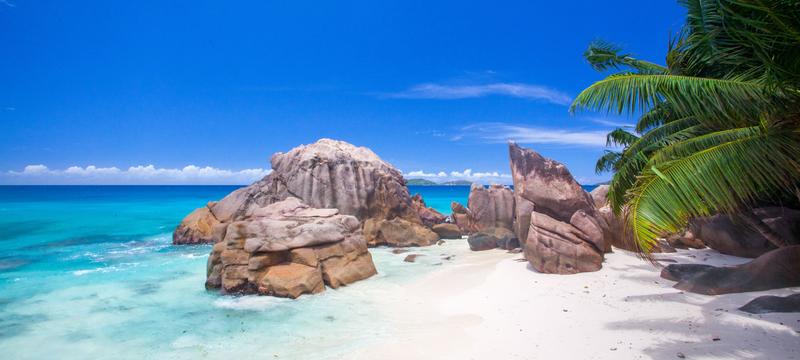 Anse La Farine Beach, Seychelles, with white sand, turquoise water, and lush greenery.