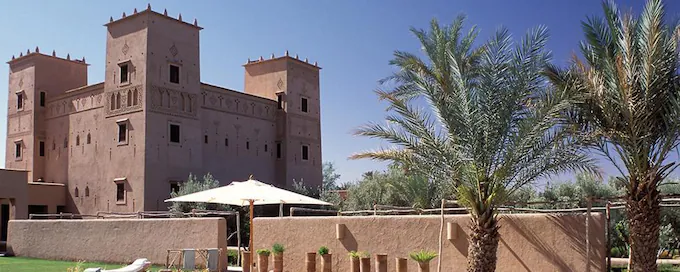  The image depicts a grand building with a vast courtyard featuring palm trees, situated at Dar Ahlam, Skoura.

