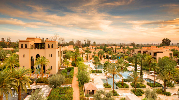A stunning sunset view of the Four Seasons Resort in Marrakech, showcasing the serene pool area and lush surroundings.
