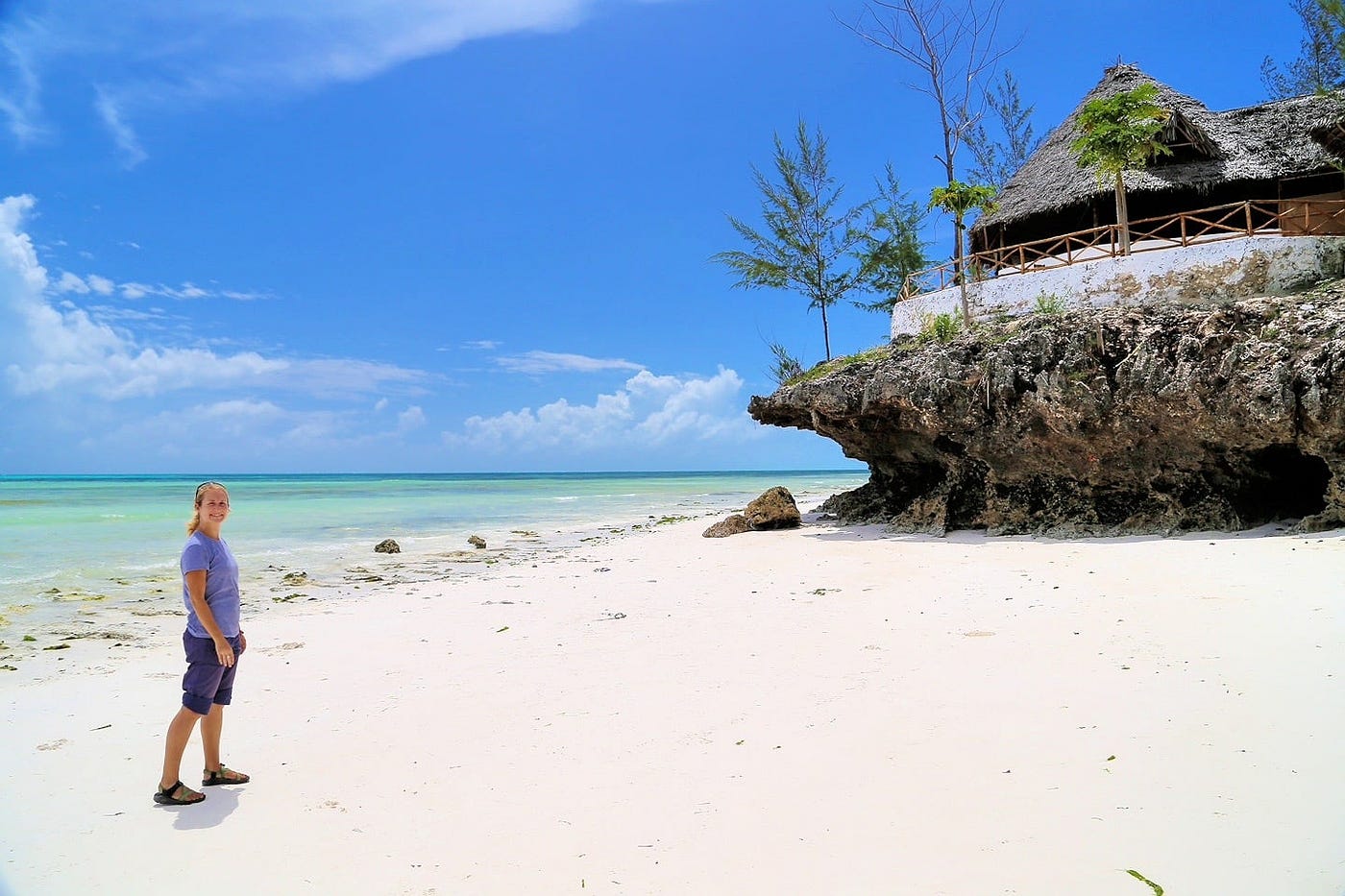  A lady stands on Jambiani Beach beside a traditional hut, enjoying the serene coastal view and gentle waves.
