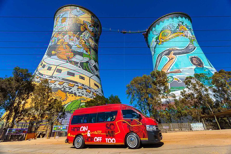 A red bus parked beside two tall towers, symbolizing the Johannesburg and Soweto Tour experience.
