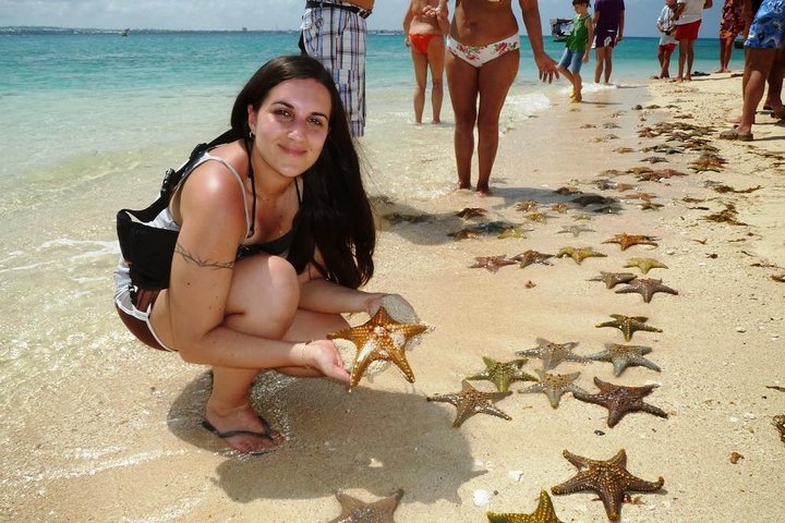 A woman kneels on Nakupenda Beach, surrounded by starfish, enjoying the serene coastal beauty of the nature reserve.