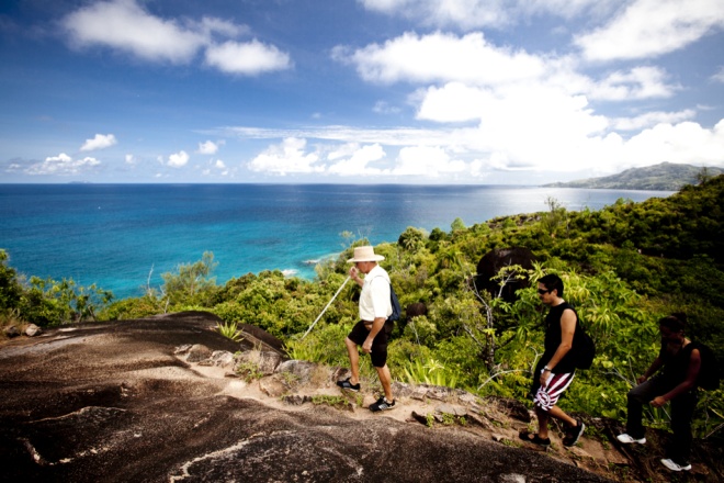  hikers ascend a rocky hill in Morne Seychellois National Park, enjoying a breathtaking view of the ocean below.
