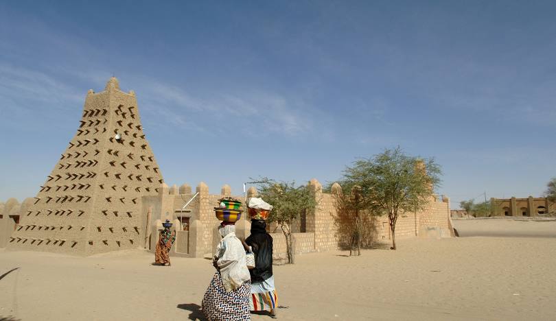Two women walking in front of a building in the desert in Timbuktu, Mali.