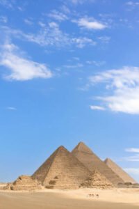 Pyramids of Giza, Giza Necropolis, Egypt: Man with camel standing in front of the Pyramids of Giza.
The Giza Necropolis is a large area near Giza, a suburb of Cairo that has many tombs and burial sites. It is also where you can find the famous Pyramids of Giza, the Great Sphinx, and more. The name comes from the ancient Greek word nekropolis, which literally means “city of the dead”.