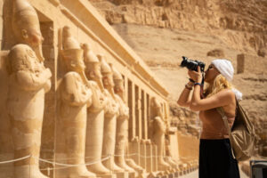 Female photographer in vacation standing with photo camera in front of the incredible Temple of Queen Hatshepsut, Luxor Egypt