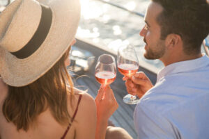 Drinking wine on yacht at sea. Romantic traveling at sunset. Happy couple in love with wineglasses enjoying summer vacation, celebration. Intimate lifestyle moment. Relaxed man and woman on sailboat.