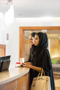 iStockalypse Dubai. Closeup of two Emirati, Arabian girlfriends wearing black abaya and waiting to check in to a spa at a luxurious hotel spa resort. Lobby in the background. Dubai, UAE, Middle East, GCC.