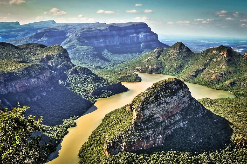 A panoramic view from a mountain summit, showcasing a winding river below amidst lush greenery.
